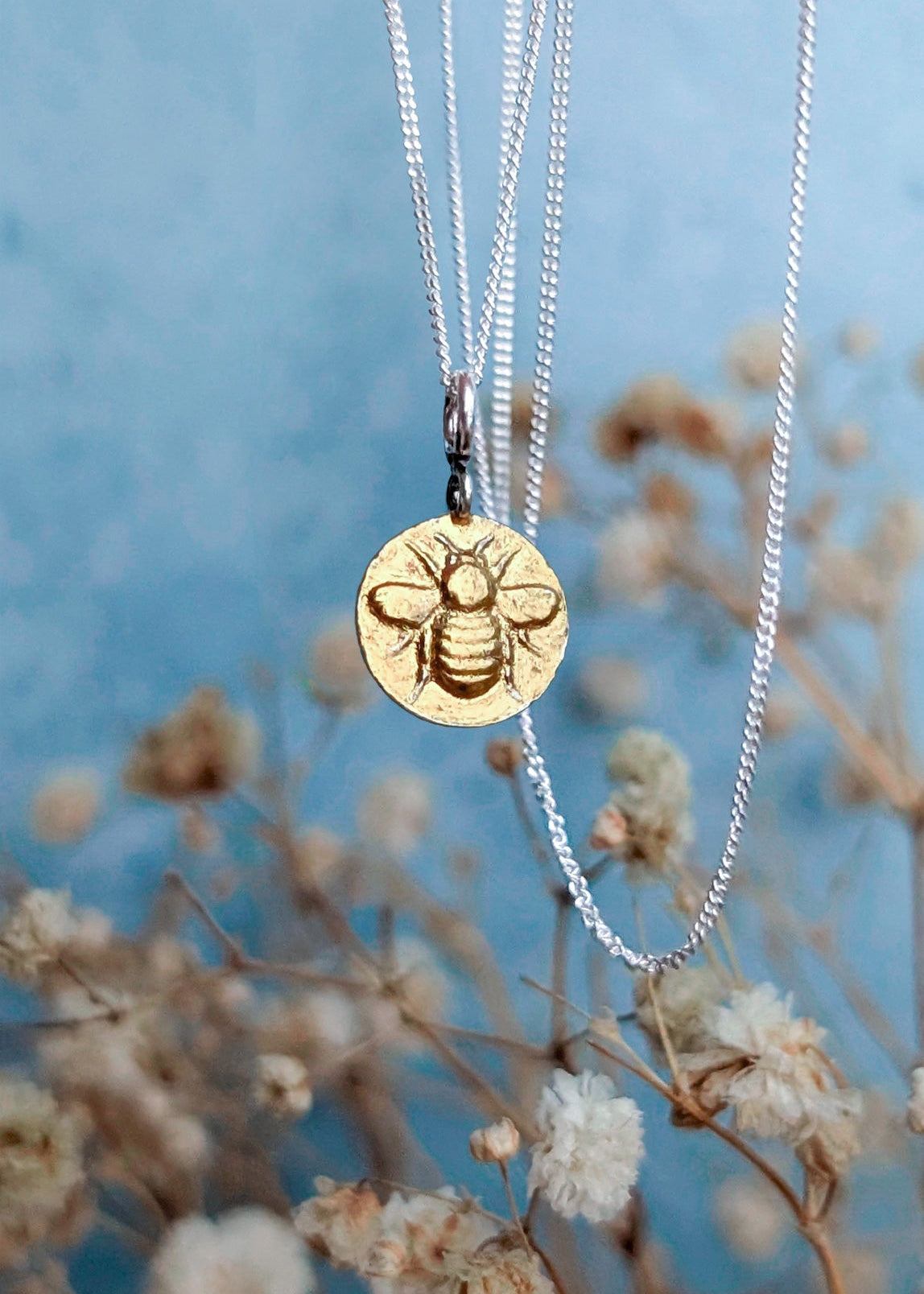 Keum boo technique 24ct gold foil coated bumblebee necklace photographed hanging in front of soft summer floral buds and a blue sky background