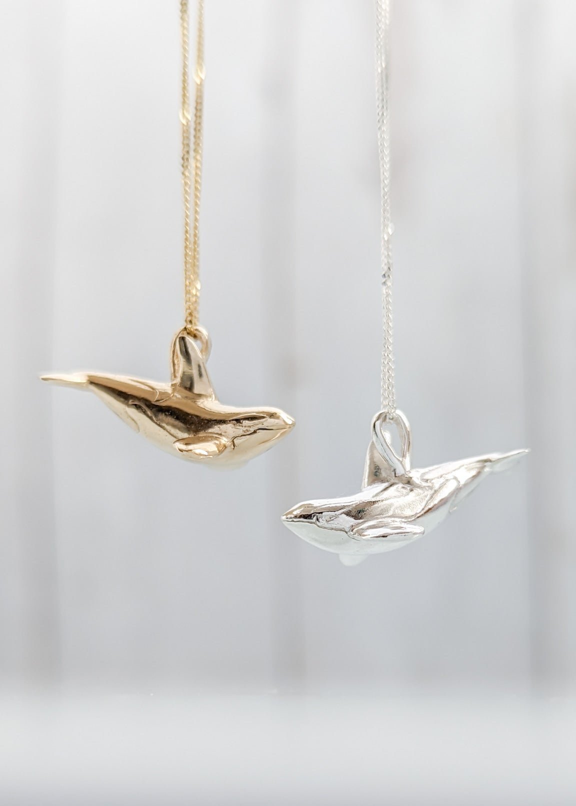 A gold and a silver orca pendant on white backdrop