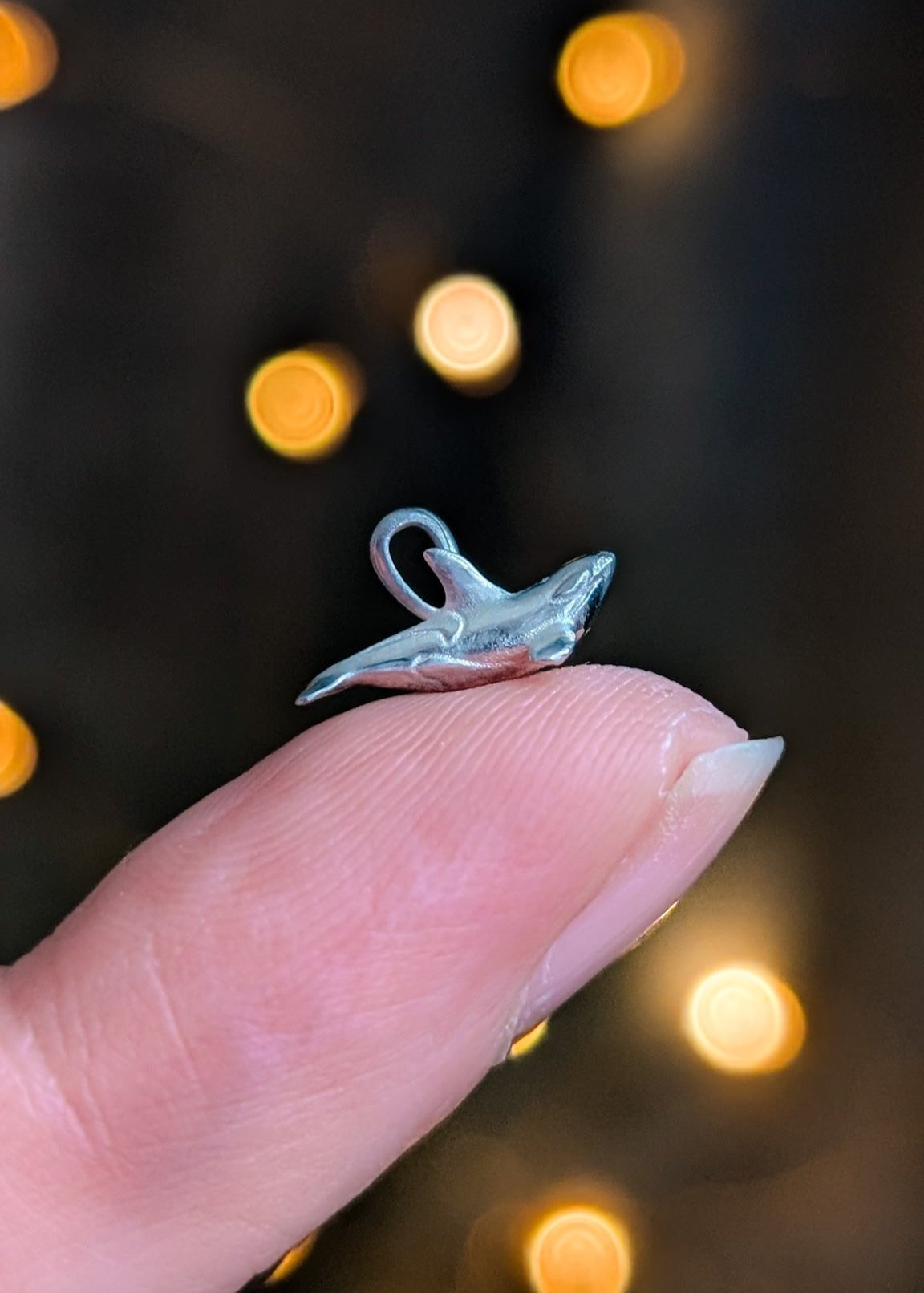 A tiny silver orca charm resting on the tip of a finger