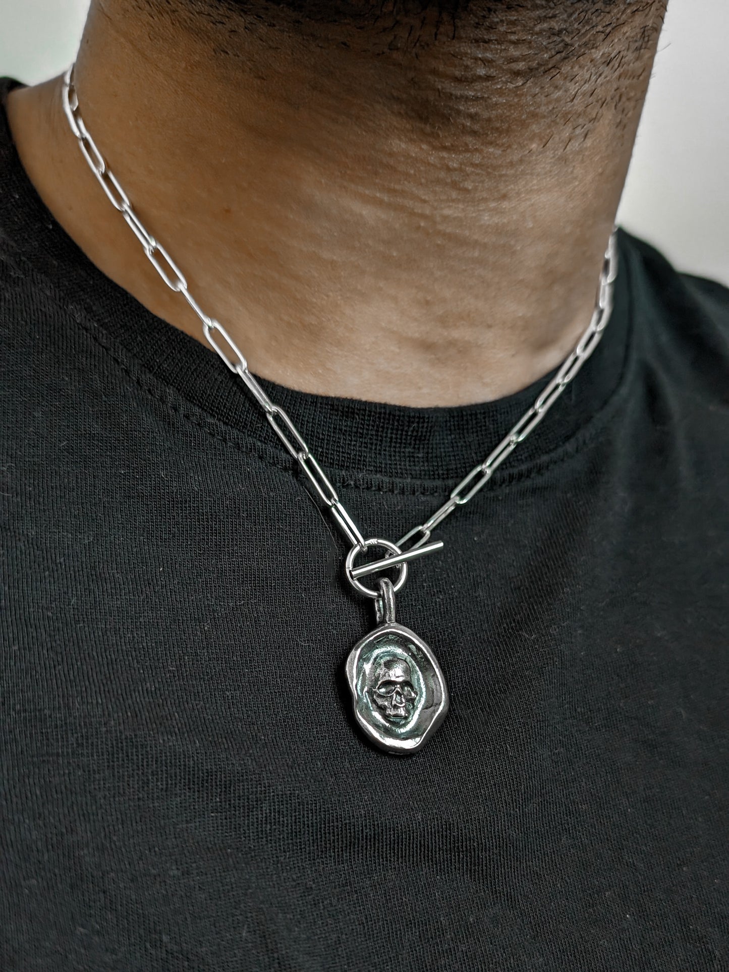 A men's wax seal skull silver necklace resting on the black cotton shirt of a male model