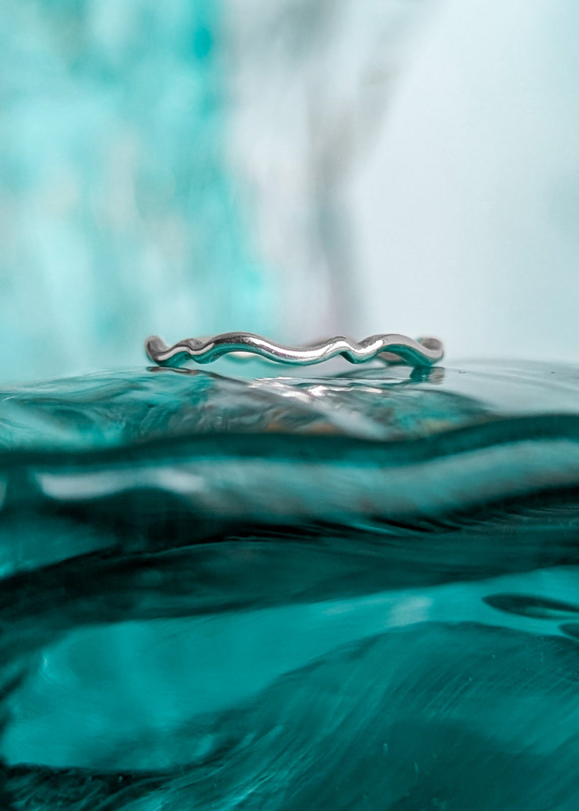 A dainty silver wavy ring that appears to be floating on top of an ocean wave
