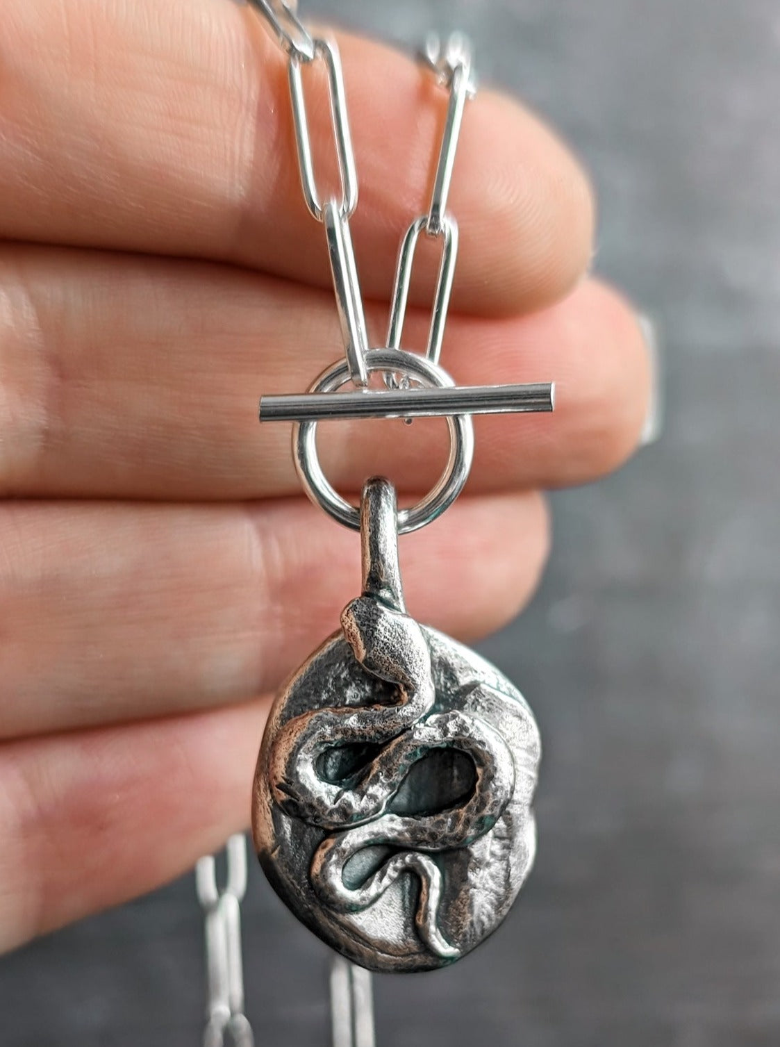 A Reputation era inspired silver snake necklace hanging from a hand to show the size