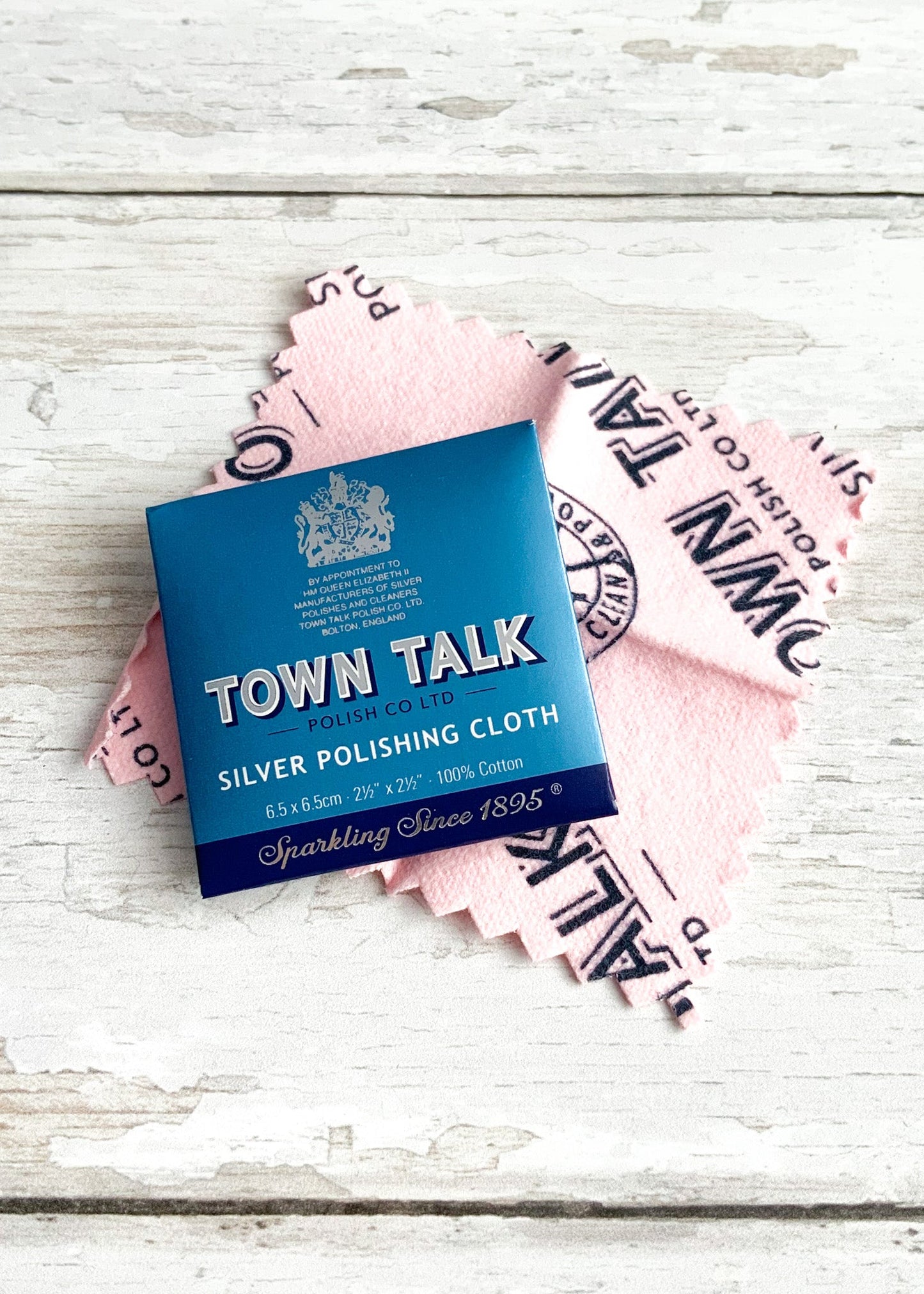 Blue sachet packaging for a Town Talk silver polishing cloth, with the soft pink cloth pictured behind