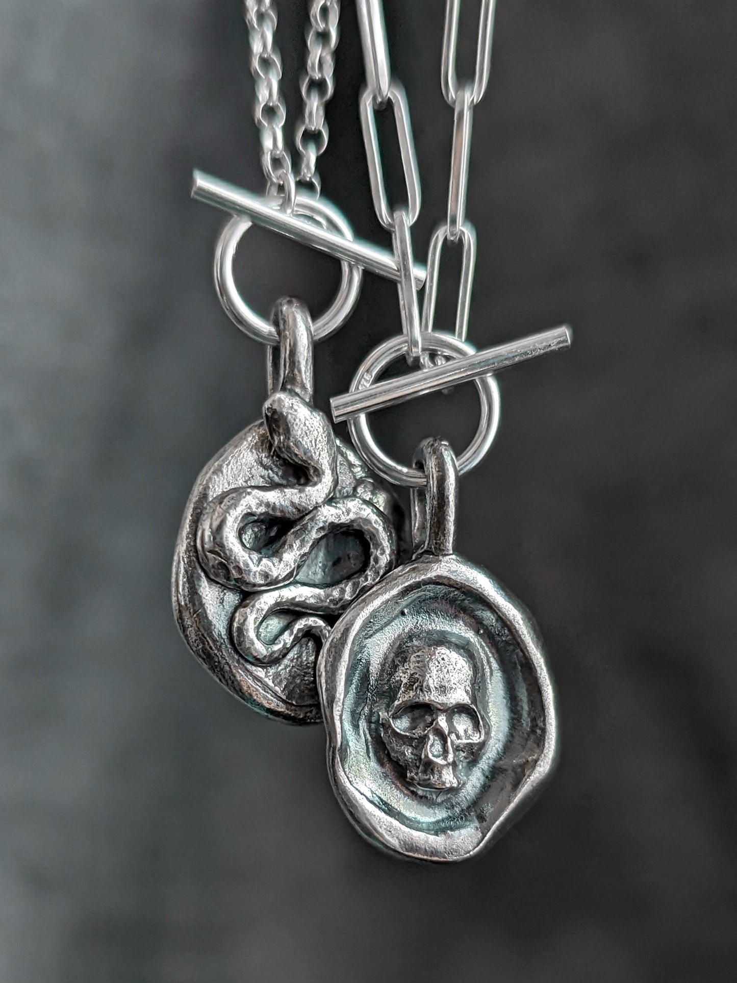 The two sides of a reversible gothic snake and skull necklace pictured together in front of a dark grey background