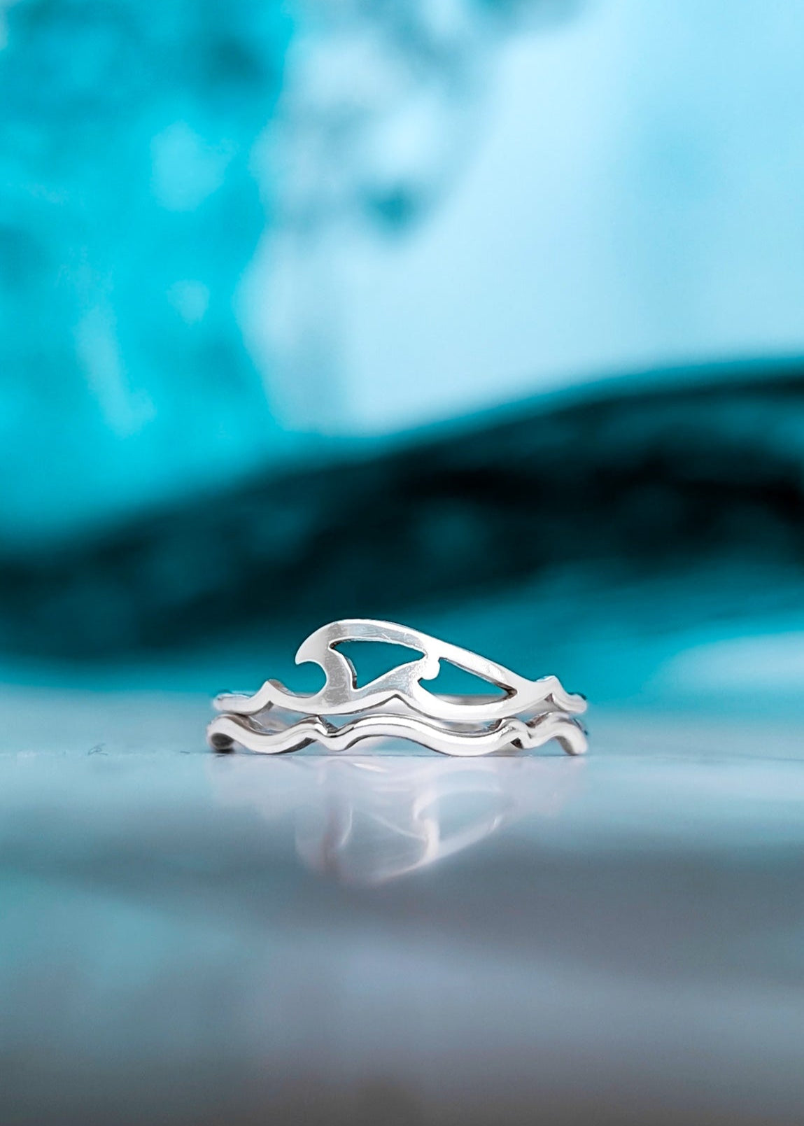A stack of two pretty silver wave rings pictured in front of an ocean blue wave cresting