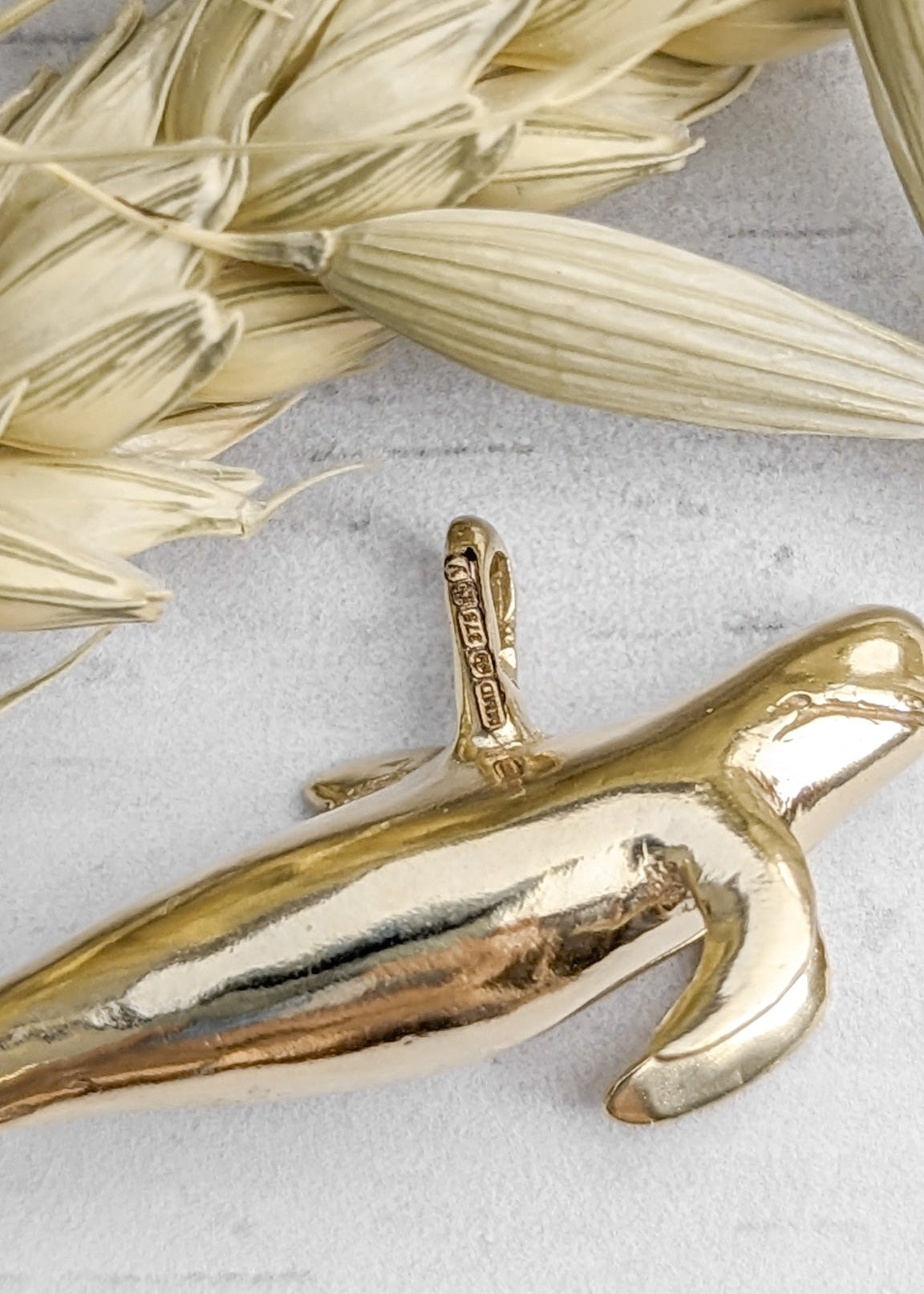 Closeup of a gold pilot whale charm featuring Hallmarks from the Edinburgh Assay Office to prove its carat
