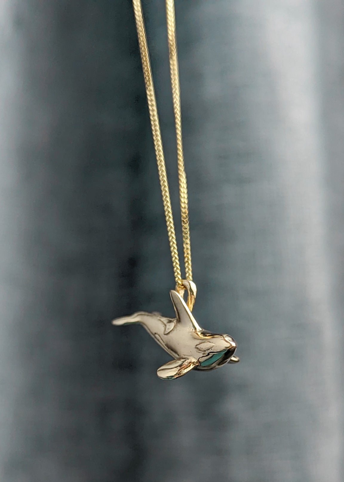 An accurate miniature orca necklace hanging in front of a textured cool grey background