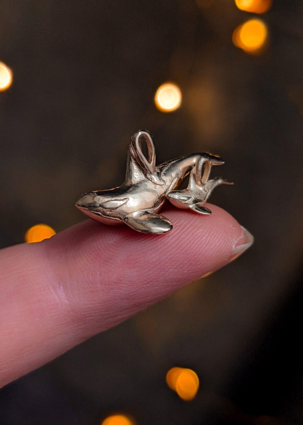 Mum and baby orca pendants in gold on a warm bokeh lights background