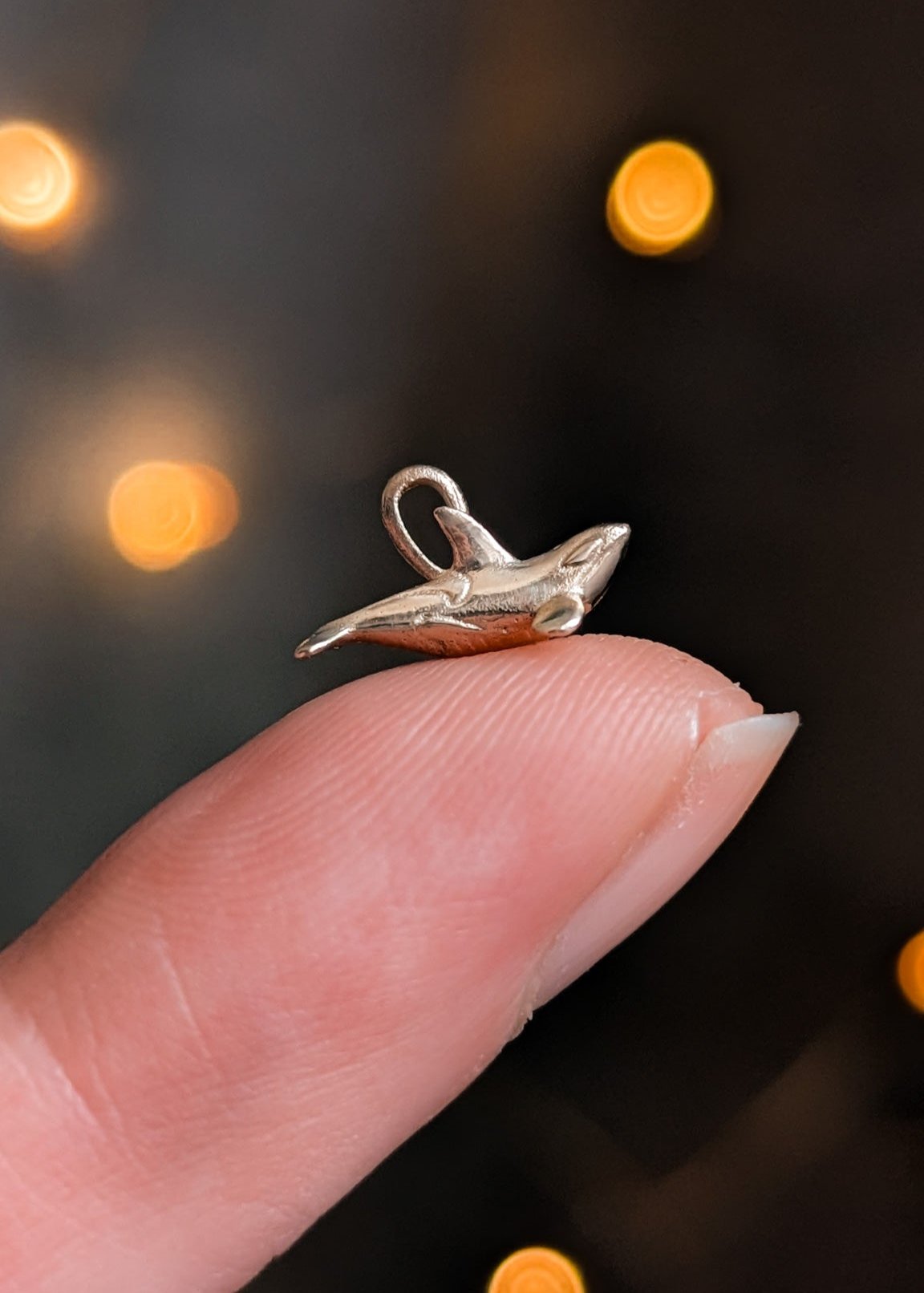 A tiny gold orca charm resting on the tip of a finger