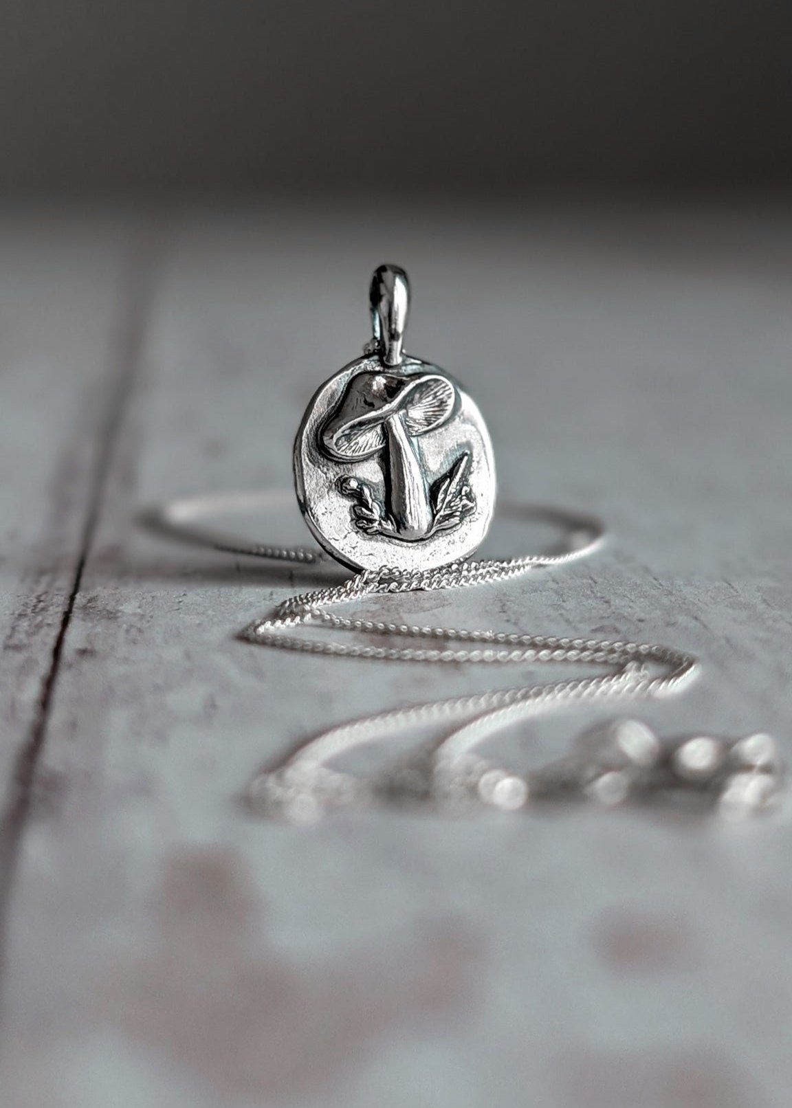 Silver oval disc pendant featuring a raised toadstool mushroom