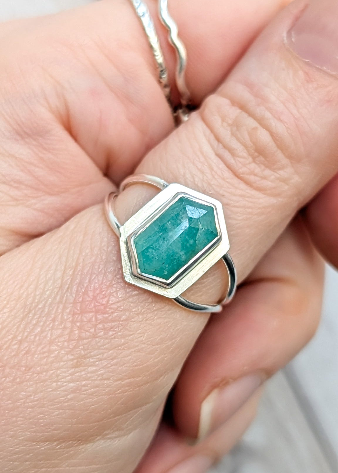 Close up of a hand, the thumb is wearing a split band silver ring with a seafoam green oblong hexagon stone set in the centre