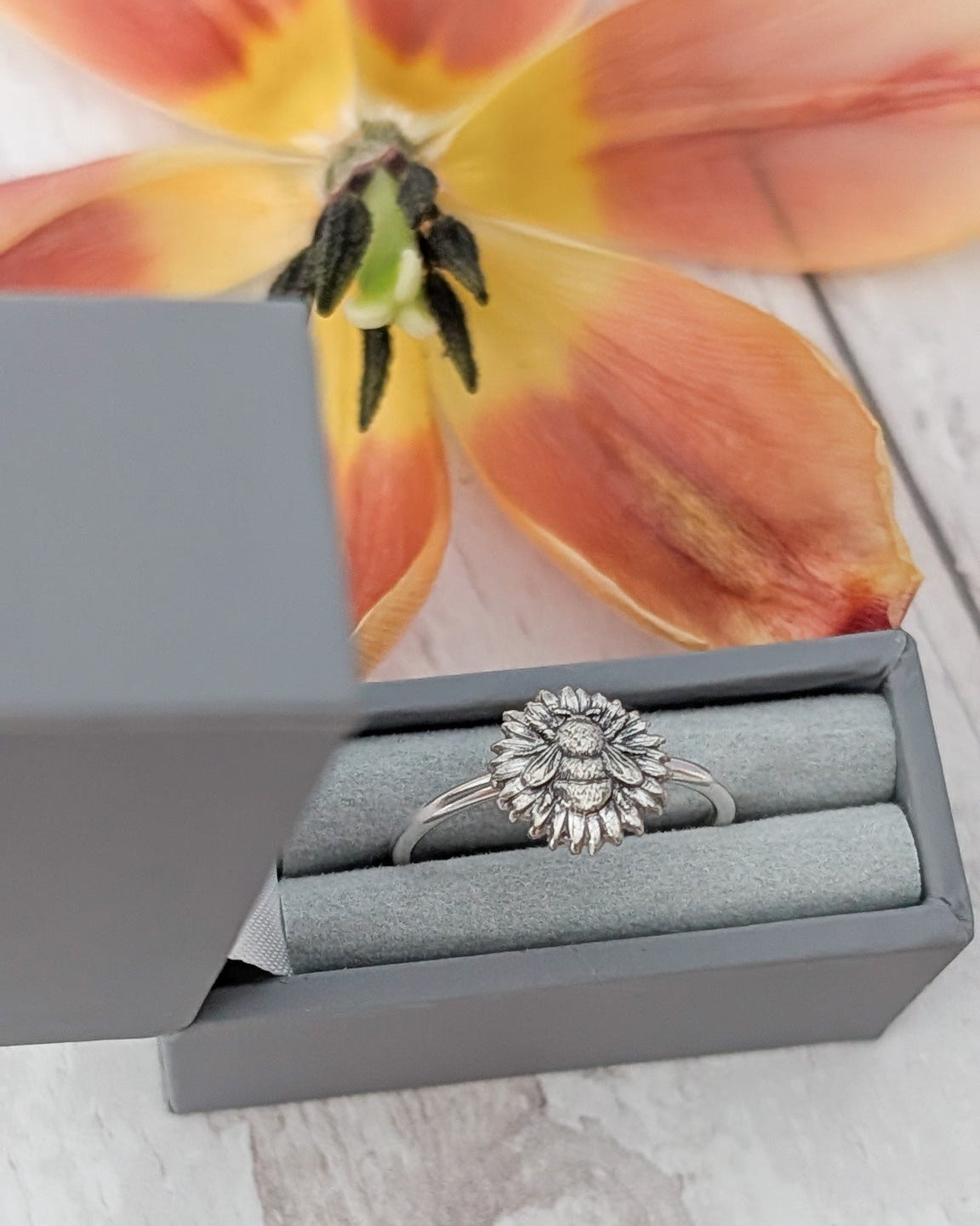 Silver bee and flower ring in a gray jewelry box with a tulip flower in the background