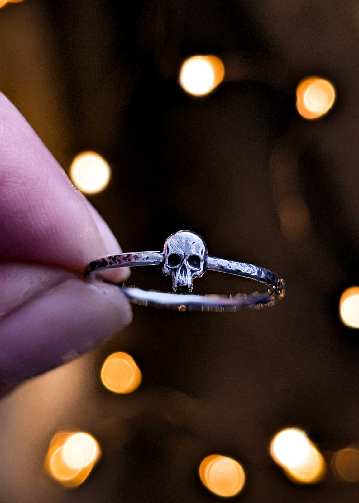 Shiny silver skull ring held by a hand with blurred lights in the background