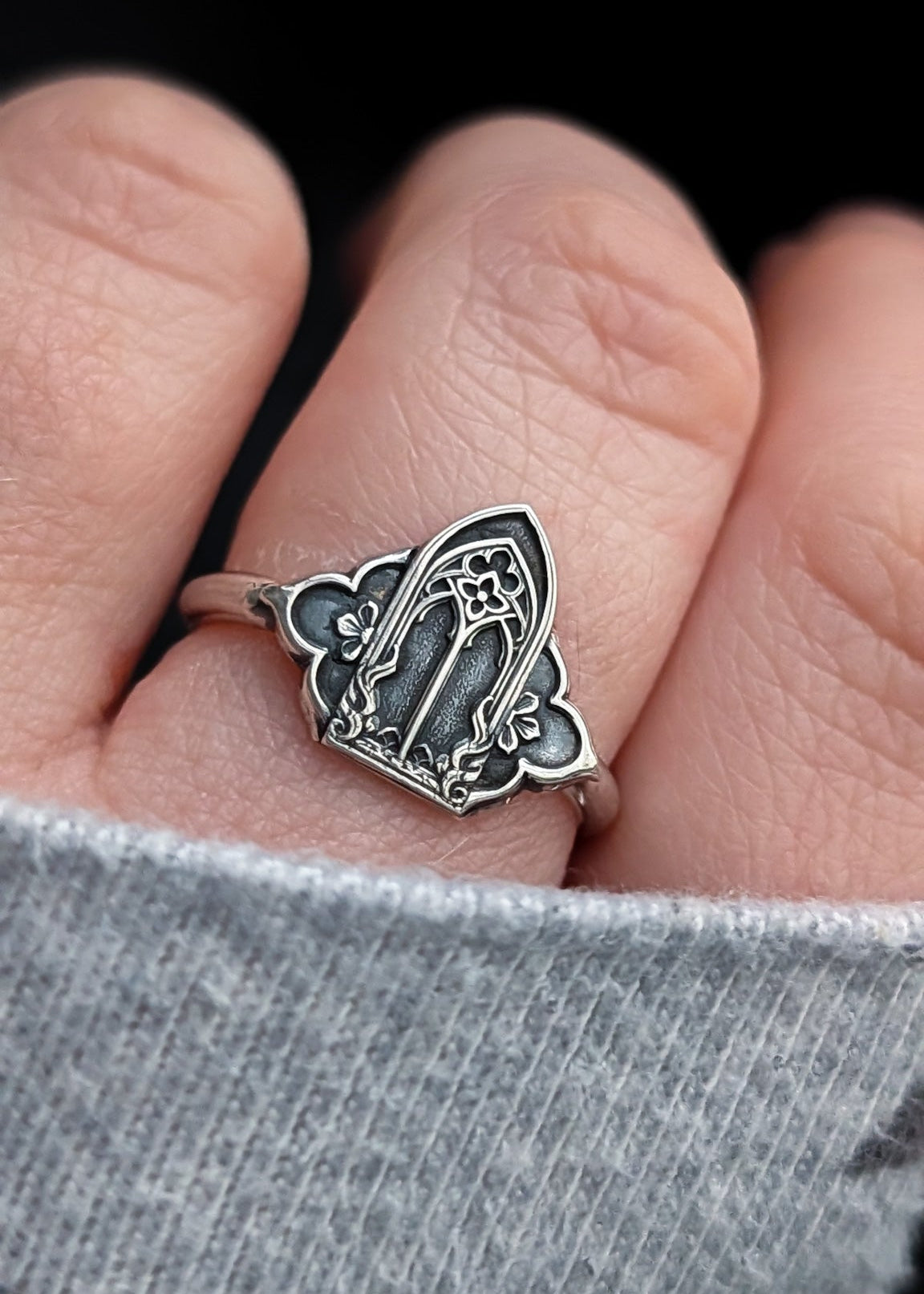 Close up of a hand wearing a darkened silver gothic cathedral window ring on the middle finger in frame