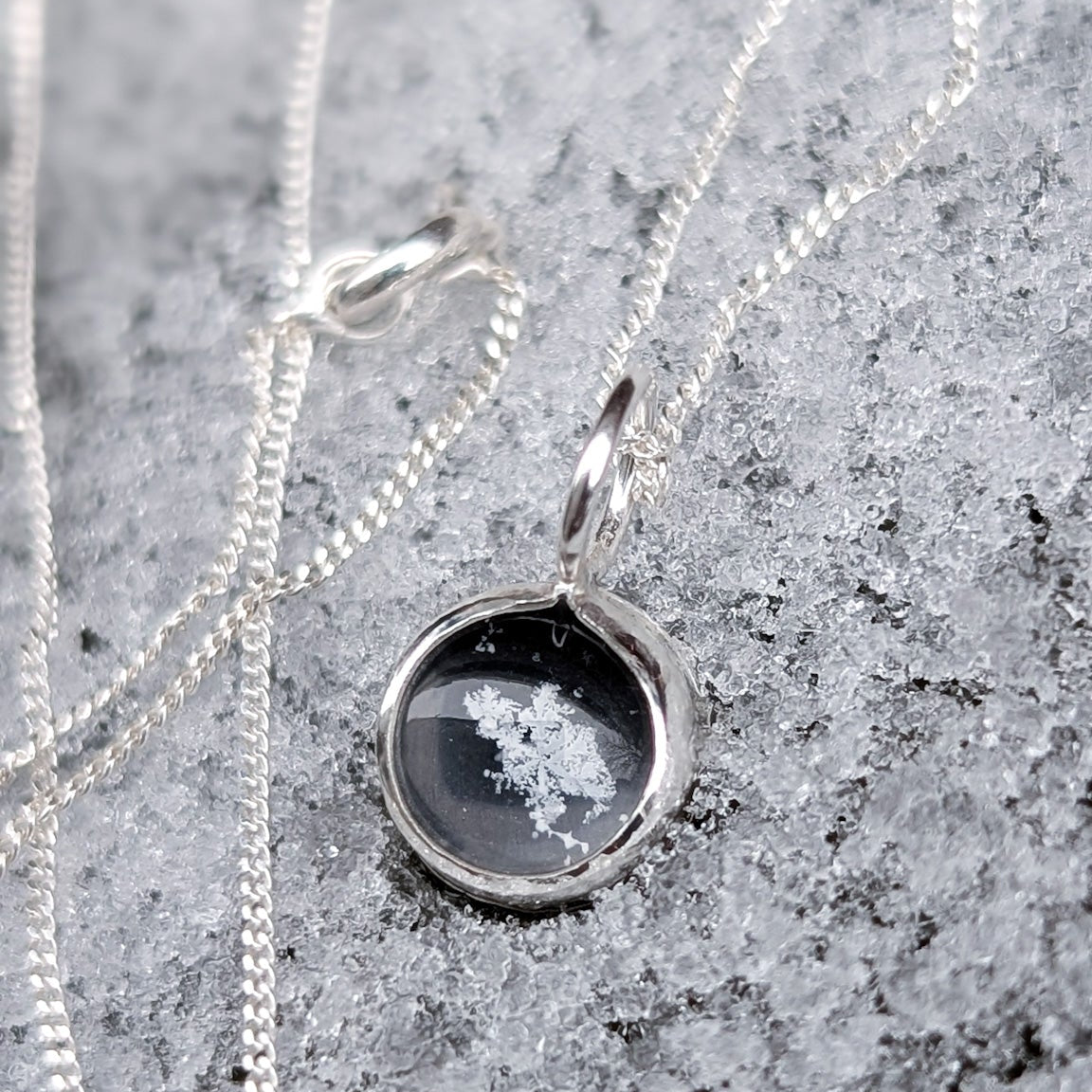 Black bead pendant with a real preserved snowflake in the centre, photographed on a snowy background