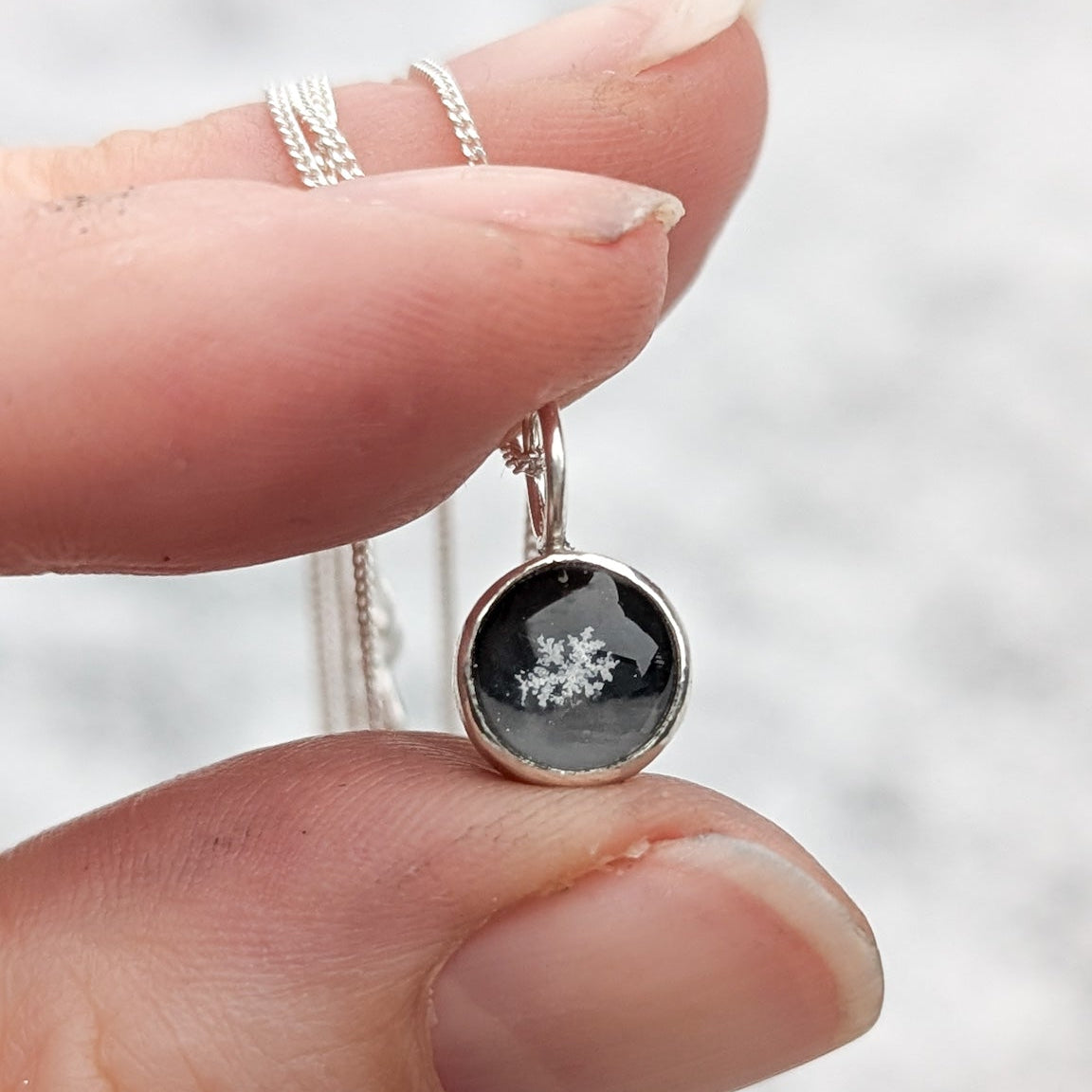 Closeup of a hand holding a tiny preserved snowflake charm. The charm is round and black with the snowflake in the centre.