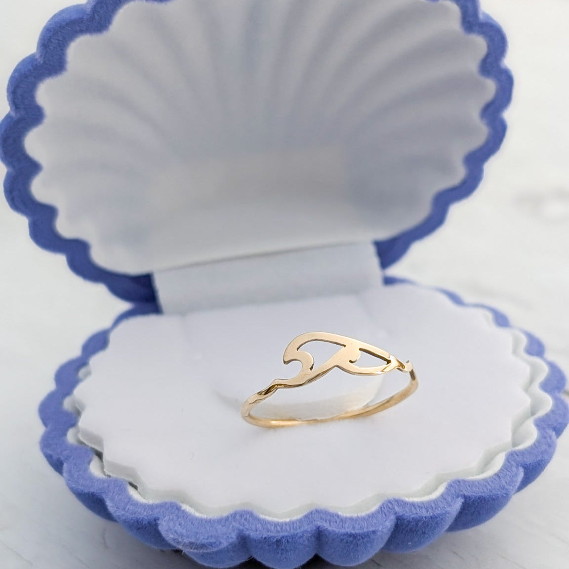 A petite gold ocean wave ring sitting in a blue seashell ring box