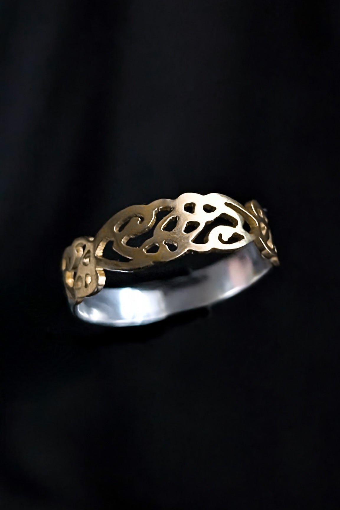 An intricate Celtic brass ring band on a dark background