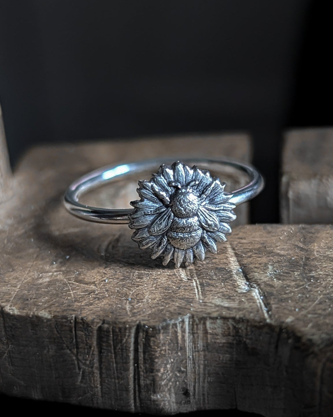 Silver ring with a bumblebee sunflower design on a wooden surface with a dark background