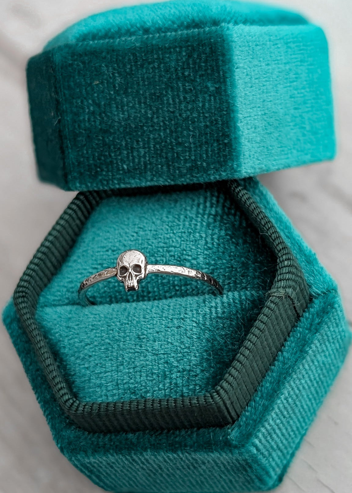 Silver skeleton face ring in a teal velvet ring box on a light wooden surface