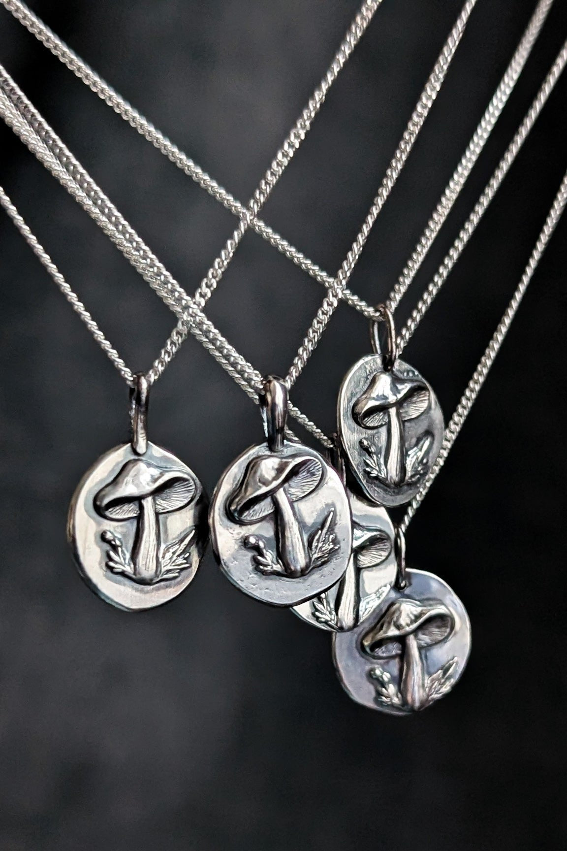 Cluster of several bright silver mushroom pendants photographed on a contrasting dark background