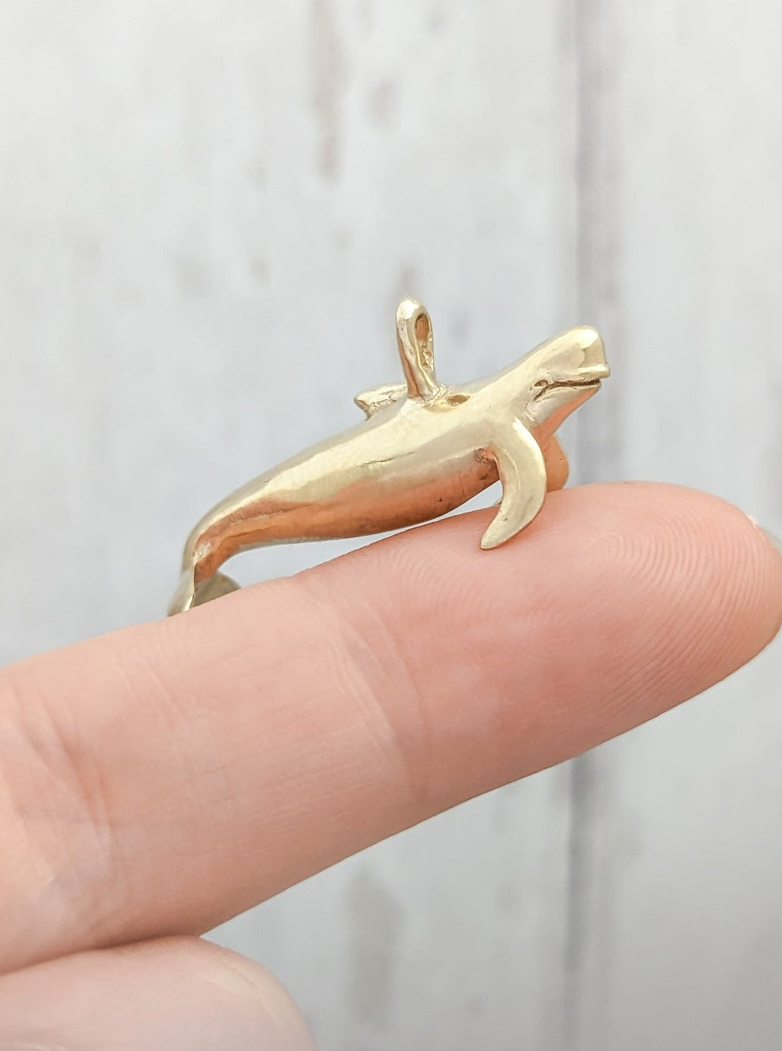Pilot whale gold charm shown on finger for scale
