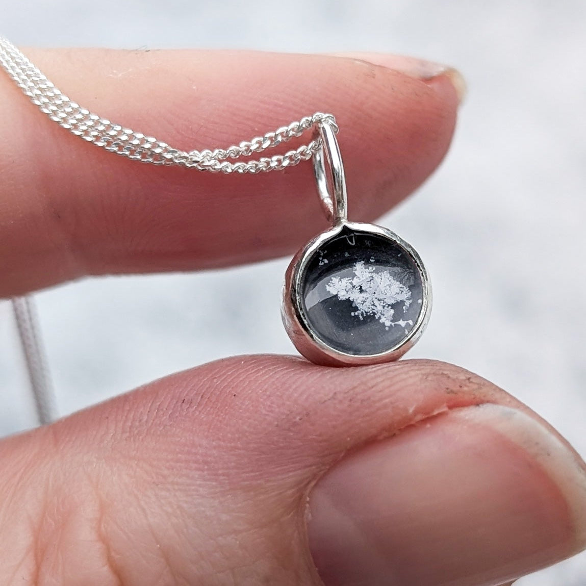 Silver genuine snowflake necklace held by a hand against a blurred white background