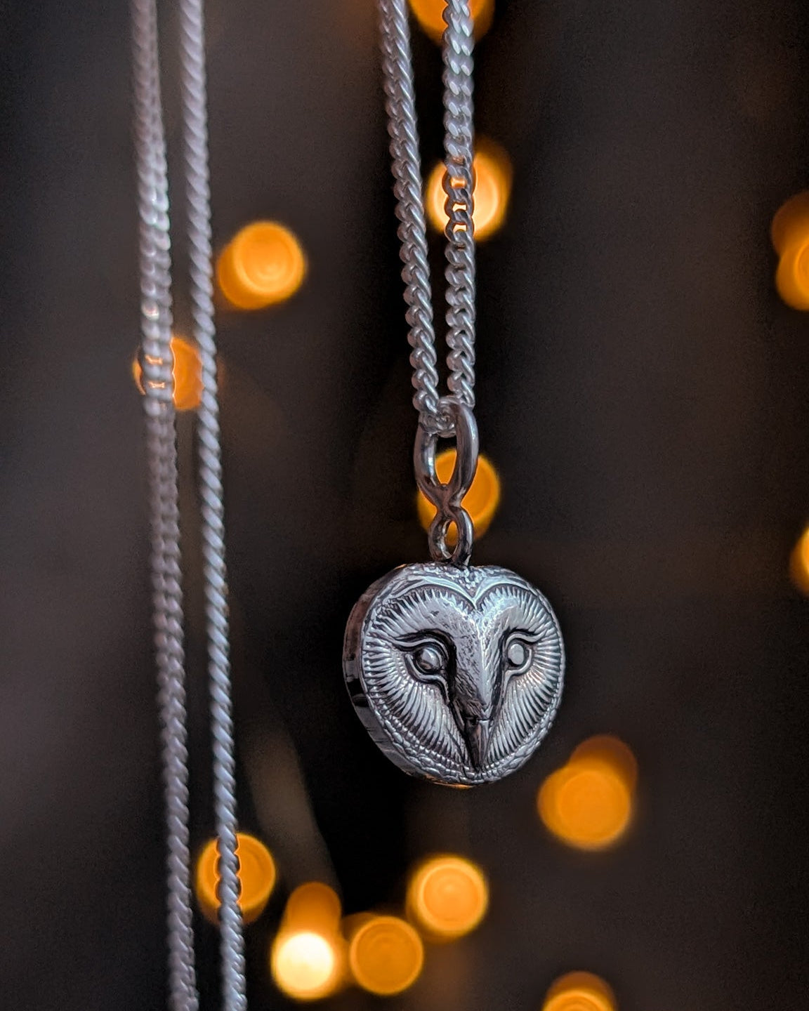 Necklace with a heart-shaped barn owl face against a blurred background with warm bokeh lights.