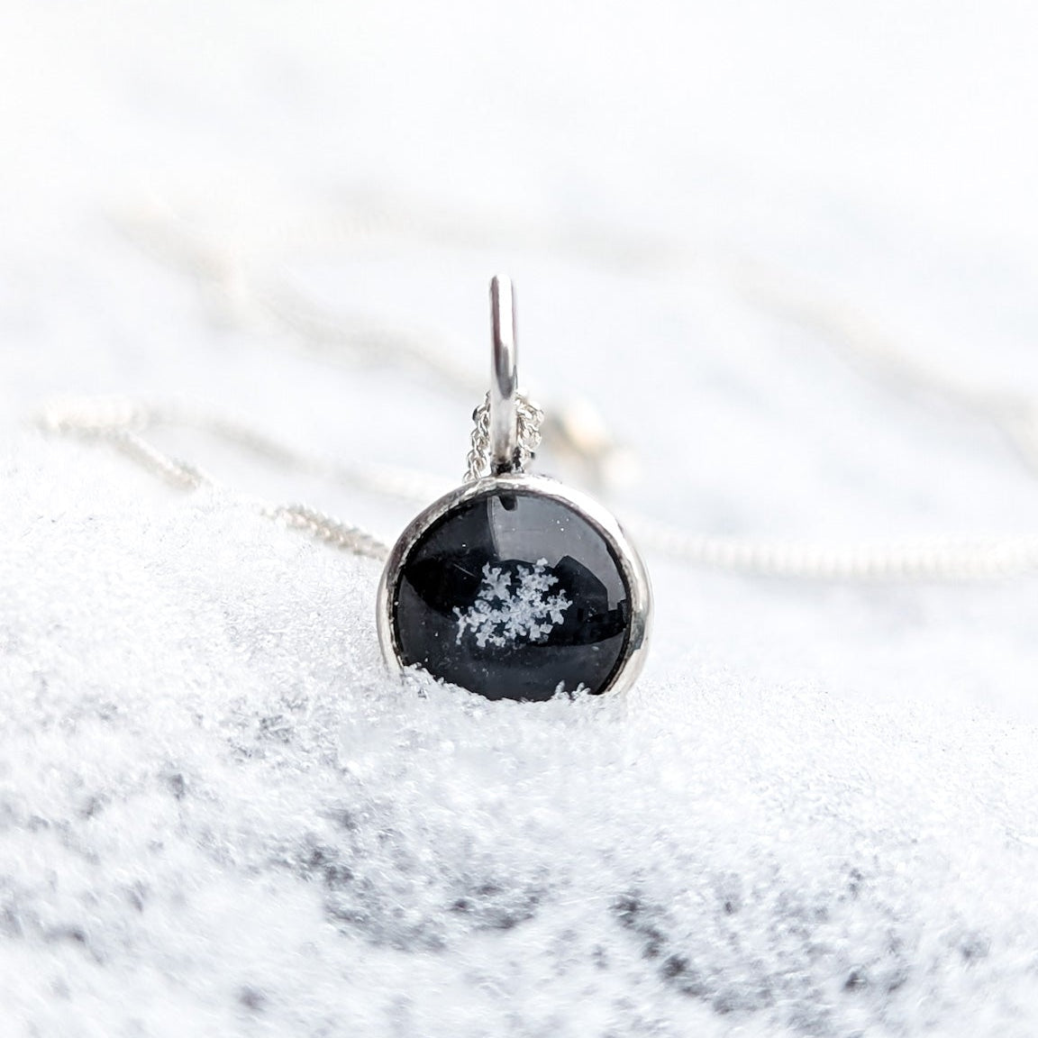 Close up of a genuine snowflake preserved on a black circle background and set in a silver pendant, photographed here on fresh snow.