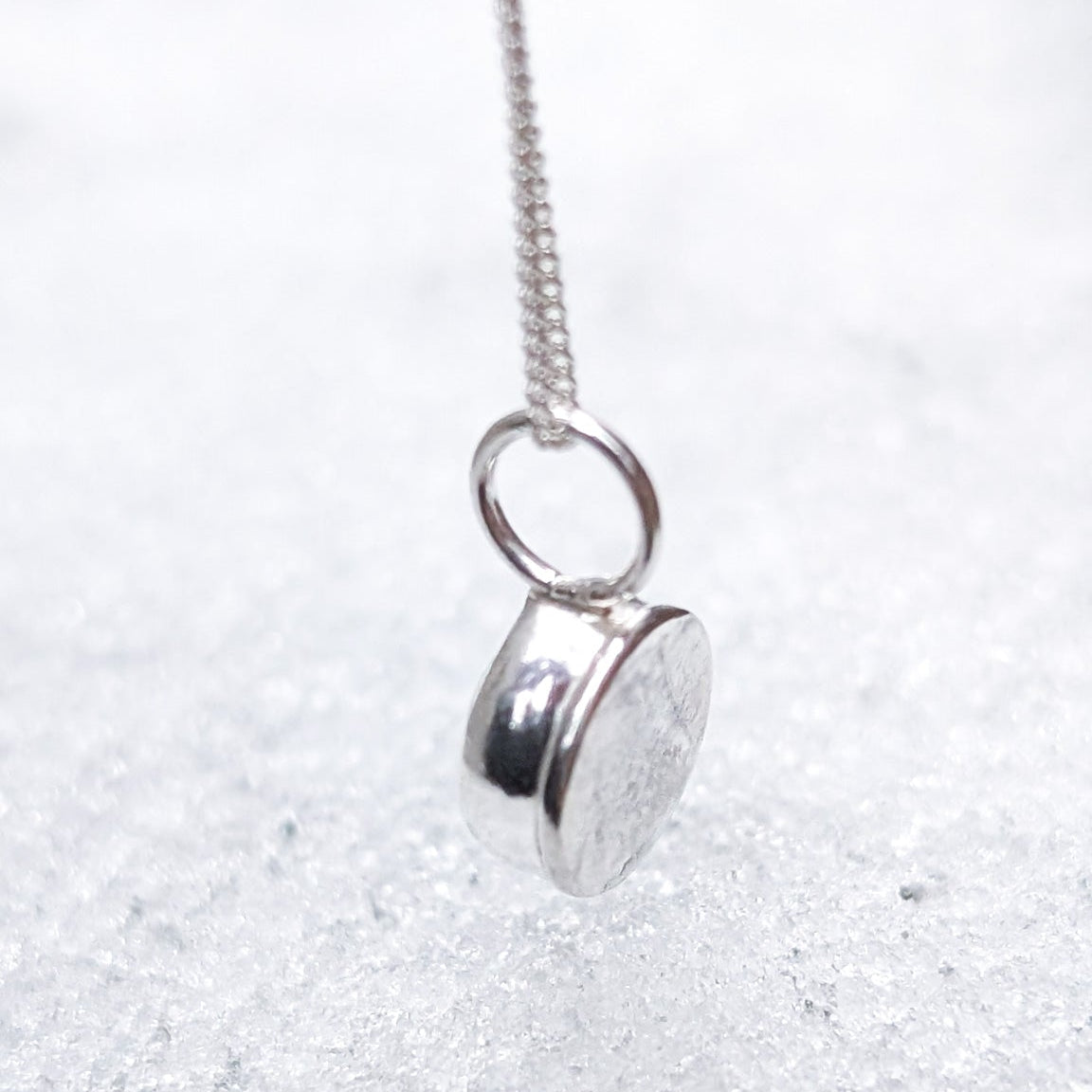 Silver necklace with a round pendant hanging over a blanket of fresh snow