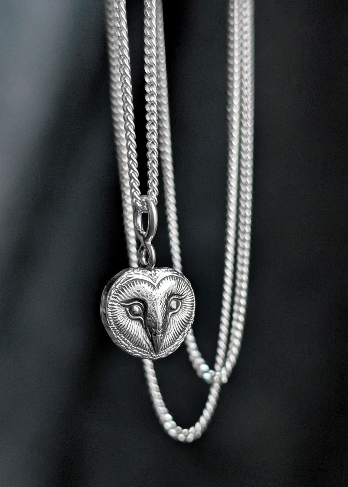 Silver necklace with a heart-shaped pendant featuring an owl face design on a black background
