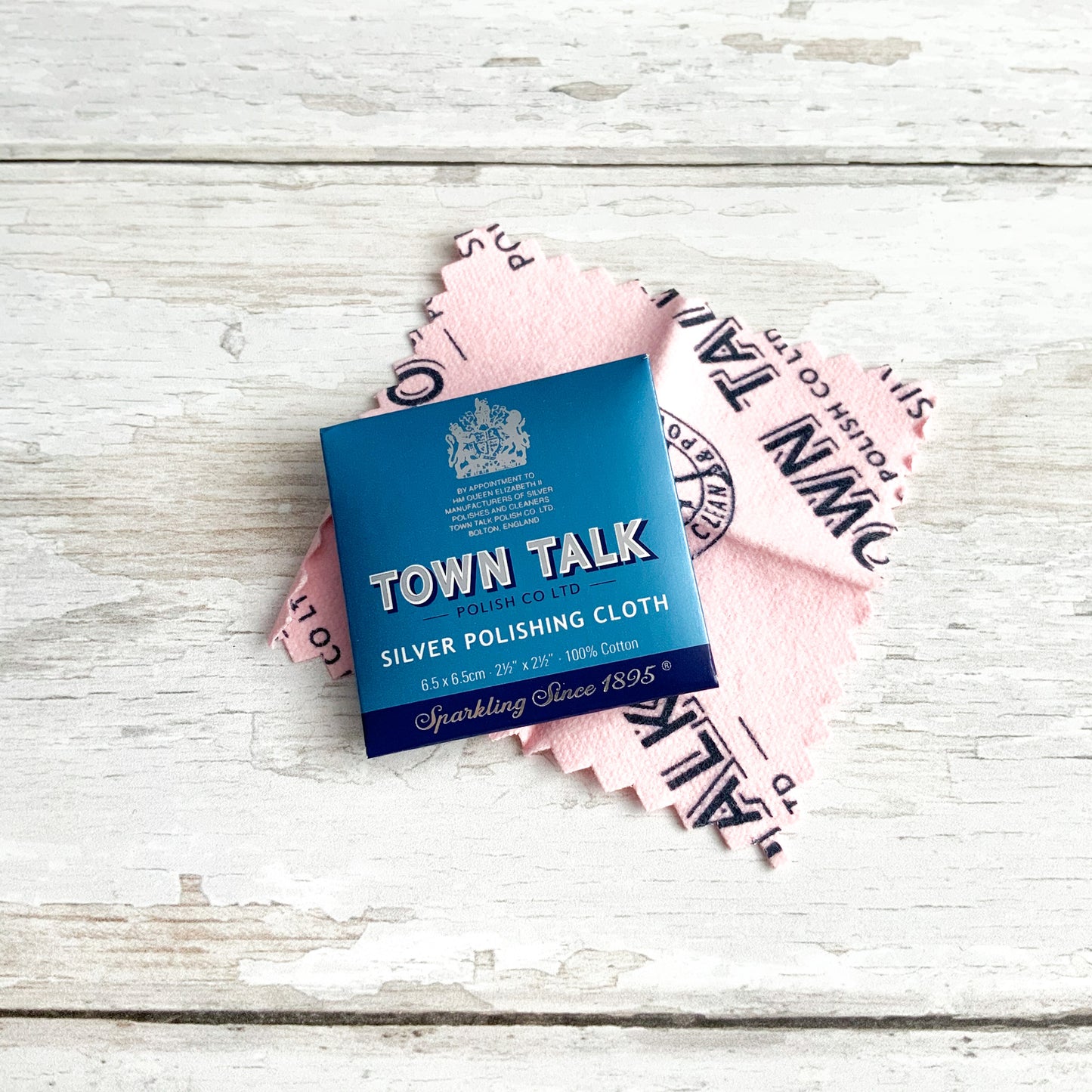 Blue sachet packaging for a Town Talk silver polishing cloth, with the soft pink cloth pictured behind