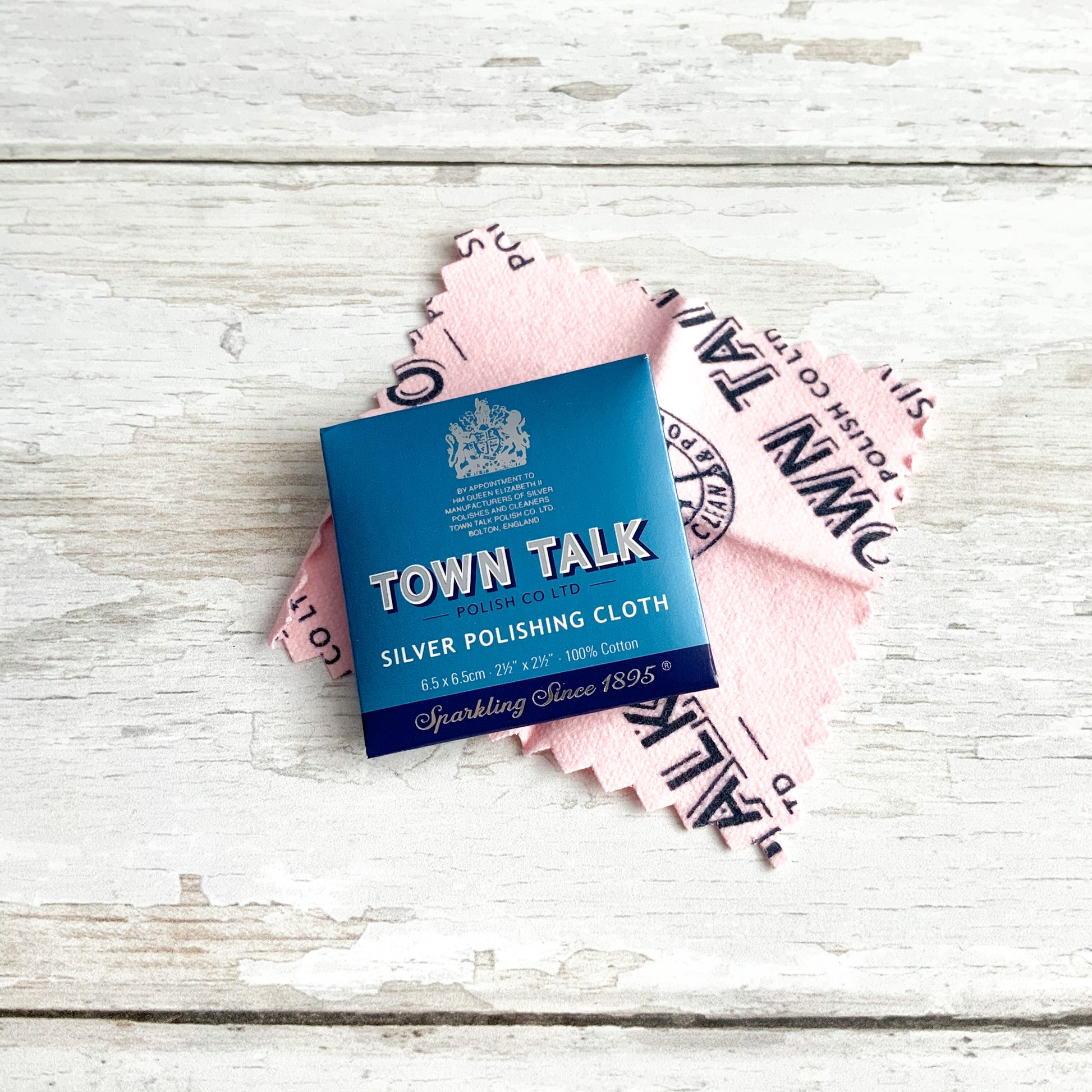 Blue sachet packaging for a Town Talk silver polishing cloth, with the soft pink cloth pictured behind