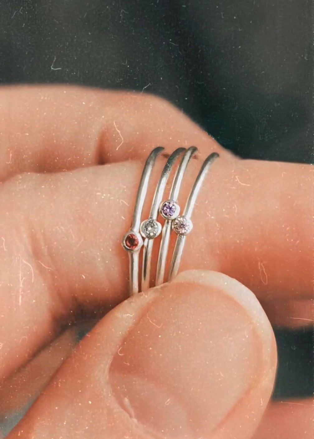 Close up of a hand with a stack of silver rings on the index finger, each with a different colour stone in the centre.