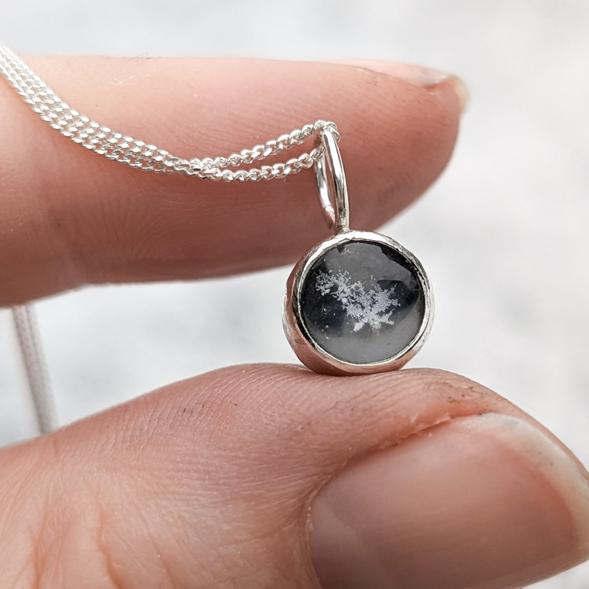 Thumb and index finger holding a round black pendant with a real snowflake inside