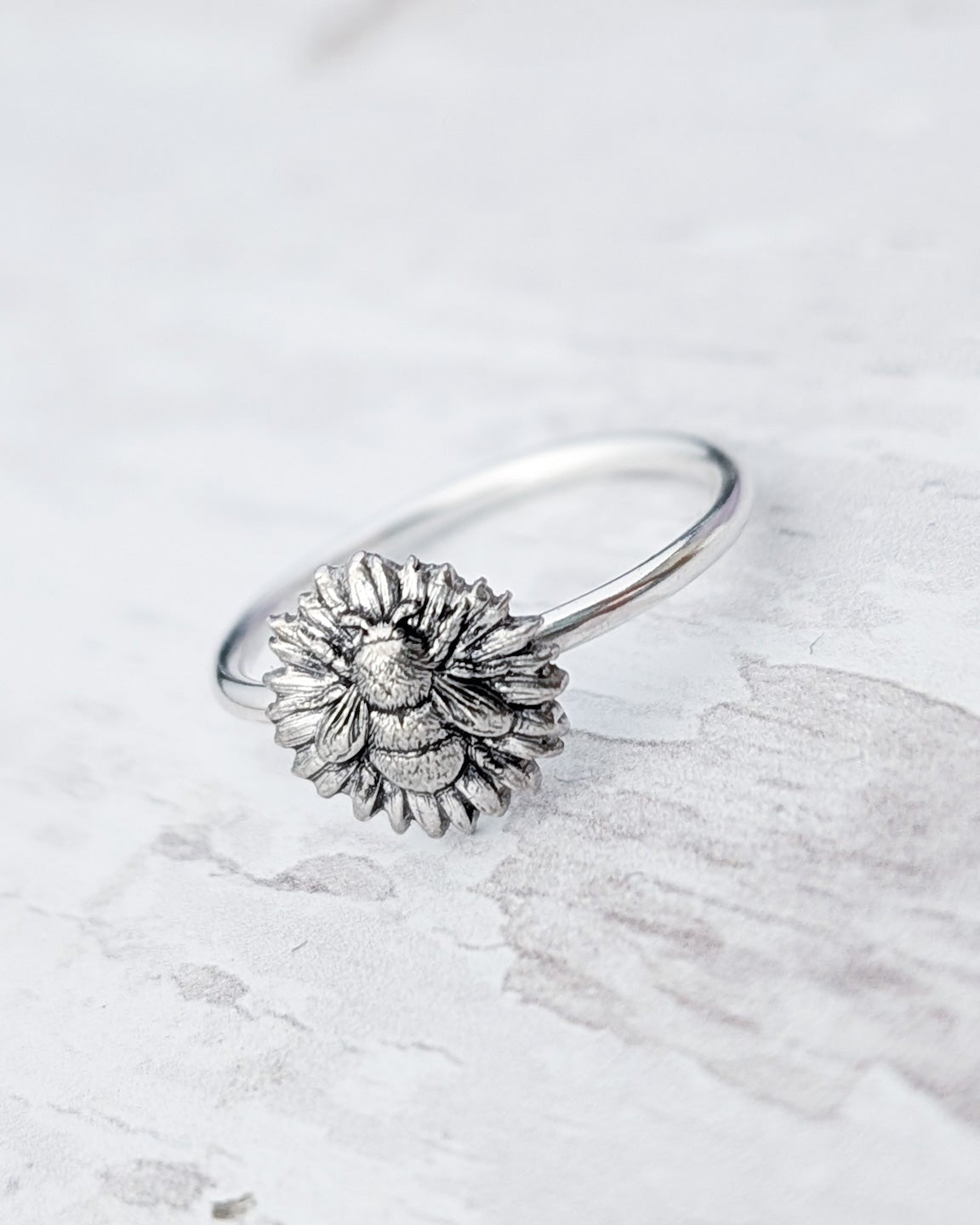 Silver ring with a daisy flower and bee design on a light wooden surface