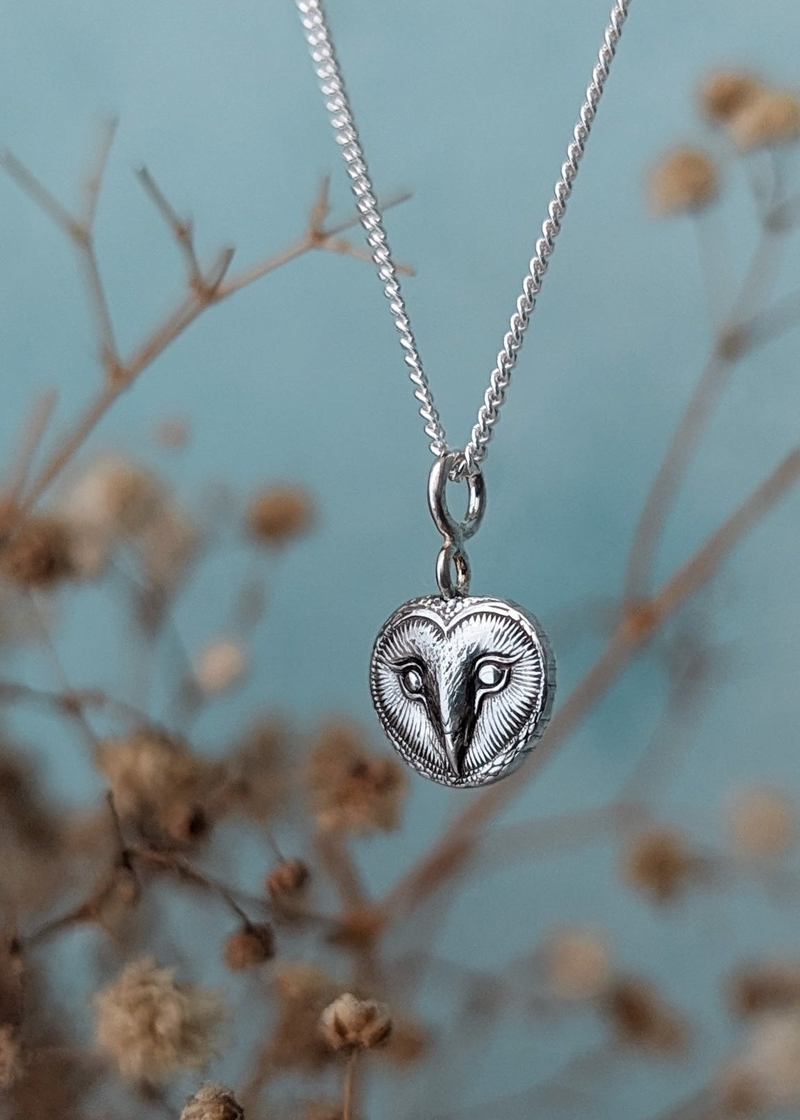 Silver owl pendant necklace on a chain with a blurred natural background