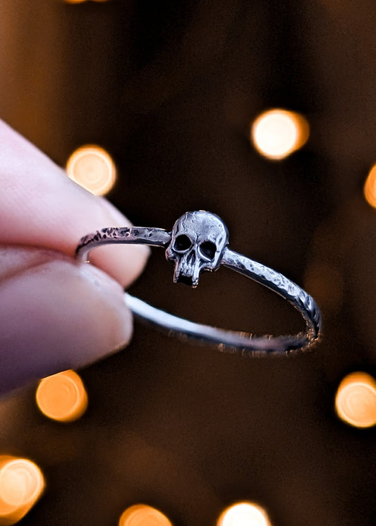 Silver skull ring held by a hand on a dark background lit by blurred soft lights