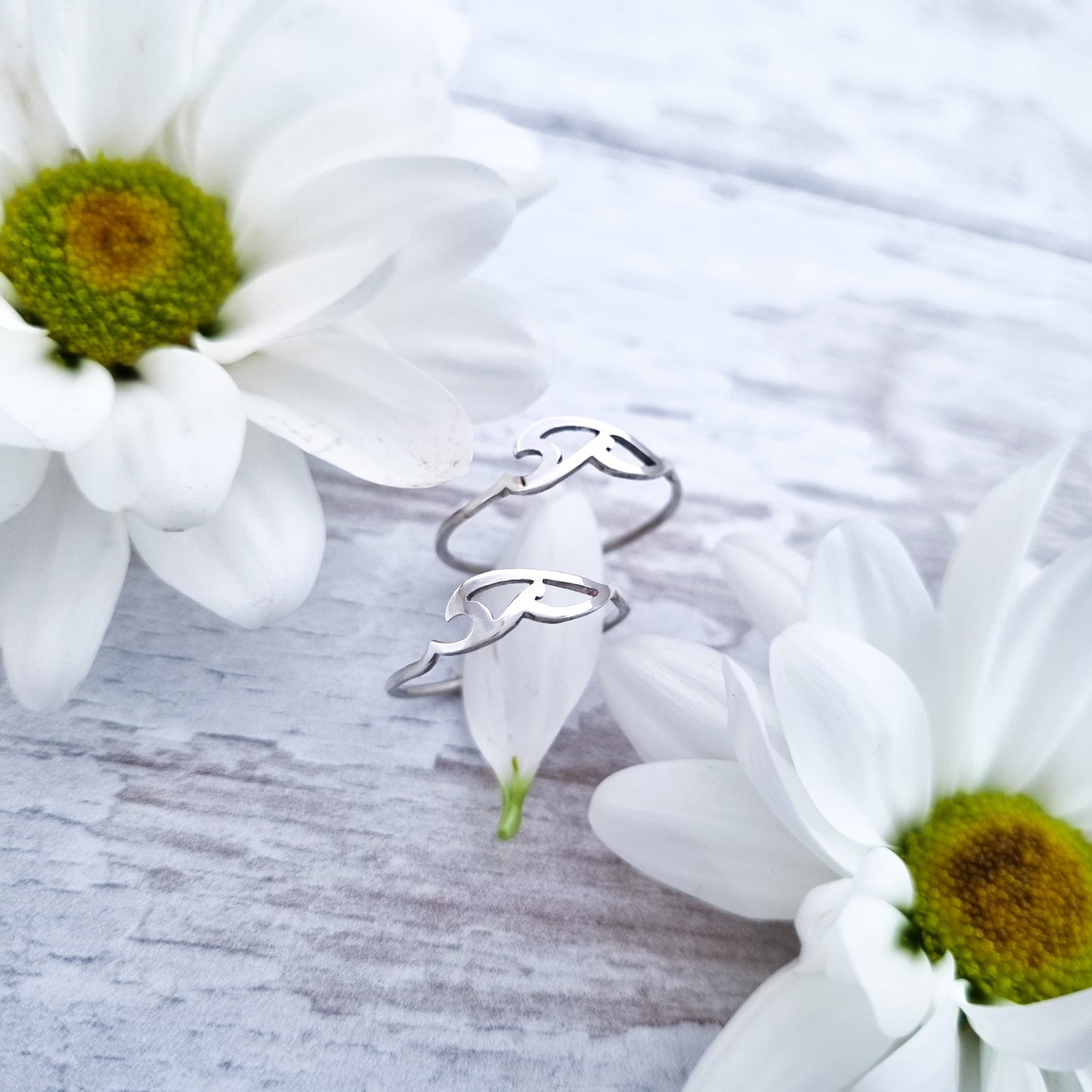 2 silver Celtic style wave rings pictured between some soft white flowers.