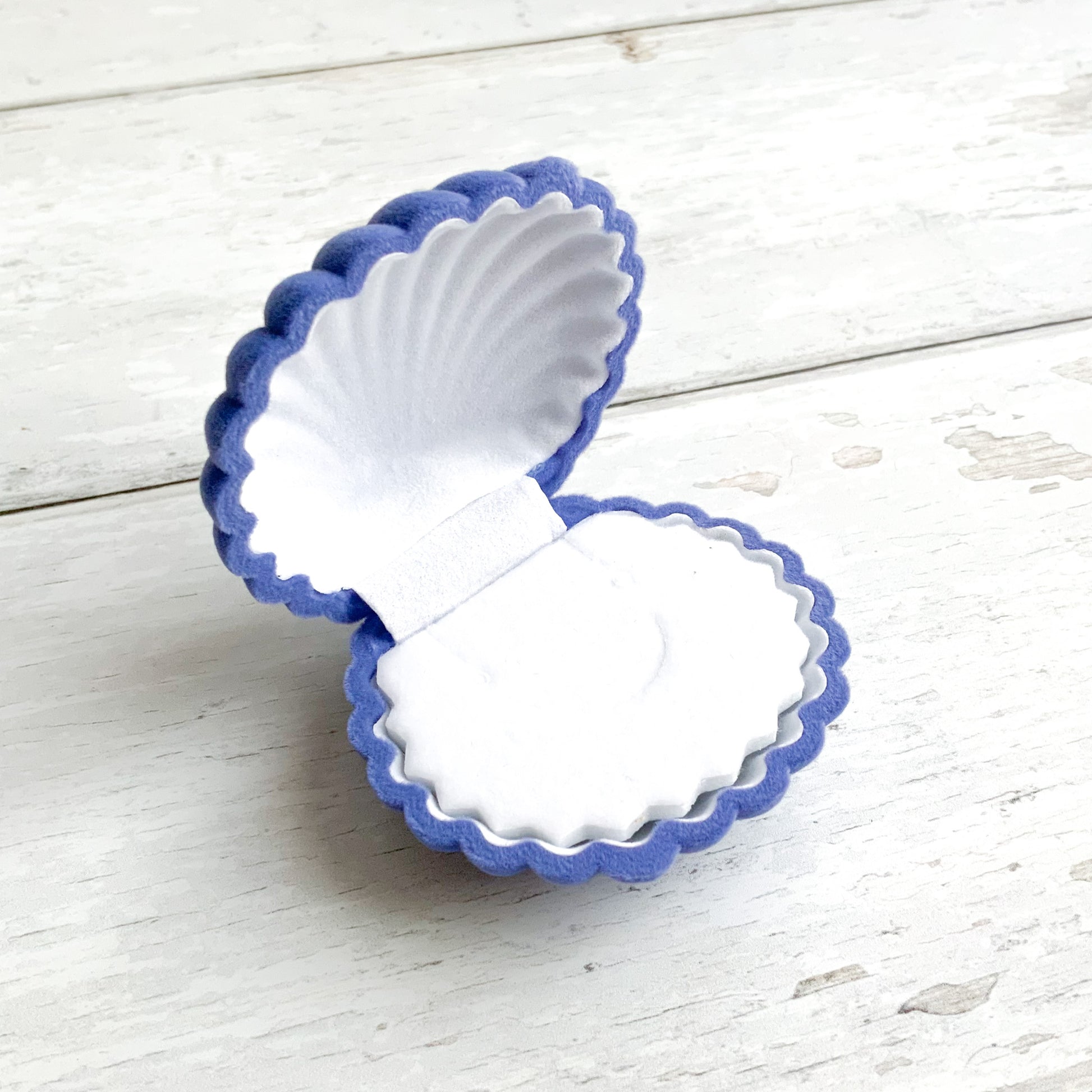 A blue shell ring box photographed open on a white wooden surface.